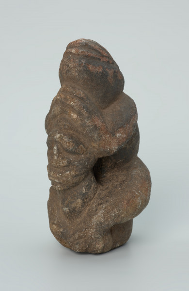 rzeźba; popiersie; Figura kultu zmarłych - Ujęcie z przodu z lewej strony. Rzeźbione w grafitowobeżowym steatycie popiersie człowieka z jaszczurką, której łapy obejmują głowę i ramiona postaci ludzkiej.