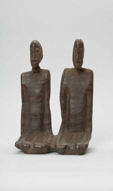 drewniana figura - Ujęcie z przodu. Para przodków siedzących obok siebie, ręce przylegające wzdłuż tułowia.