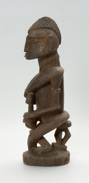 drewniana, rzeźbiona figura - Ujęcie z lewego boku. Drewniana, rzeźbiona postać kobiety, trzymającej w ramionach małe dziecko.