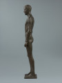 akt męski - Ujęcie z lewej strony; Rzeźba z brązu przedstawiająca nagiego, młodego, szczupłego mężczyznę, stojącego twarzą do widza z rękami wzdłuż ciała.