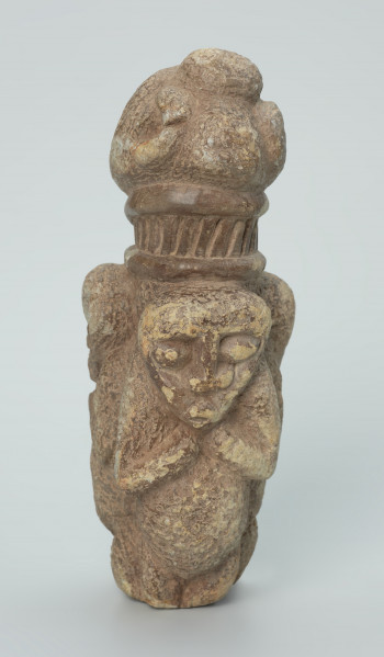 rzeźba; przedmiot obrzędowy; figura kultu zmarłych - Ujęcie z tyłu. Rzeźbiona w szarobeżowym steatycie, otoczona trojgiem dzieci, postać ludzka o cechach kobiecych z naszyjnikiem przypominającym kryzę.