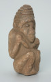 rzeźba; przedmiot obrzędowy; Figura kultu zmarłych - Ujęcie z przodu z prawej strony. Rzeźbiona w szarobeżowym steatycie postać ludzka ze spiralną linią na czubku dużej głowy, siedząca z przykurczonymi nogami i trzymająca w dłoniach bliżej nieokreślone przedmioty, kształtem przypominające motyki.