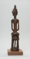 drewniana figura - Ujęcie z tyłu. Drewniana, rzeźbiona figura kobiety, siedzącej na stołku.
