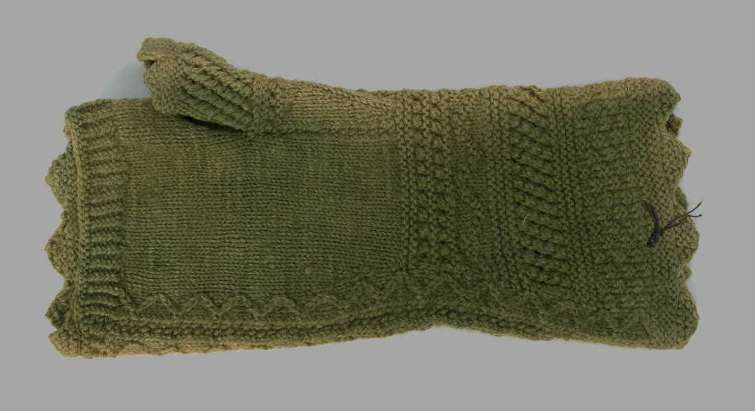 Rękawiczka bezpalcowa, z aplikacją z haftem kwiatowym - Ujęcie z tyłu; Spodnia strona rękawiczk z jednym palcem, wykonanej z zielonej wełny. Przy przegubie dłoni i w miejscu, gdzie powinny być palce wykończona w wyraźne ząbki.