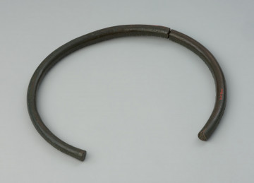 biżuteria; ozdoba ciała - Ujęcie z góry tyłu naszyjnika. Zachowany w dwóch fragmentach naszyjnik z grubego brązowego pręta, zdobiony motywem poprzecznego żebrowania.