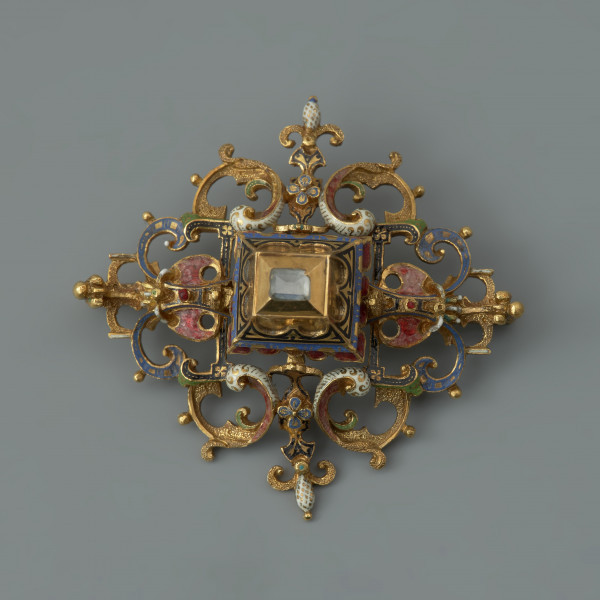 rozeta z kołpaka księcia Filipa II (1573-1618) - Ujęcie z przodu. Klejnot zbudowany z dwóch skręconych ze sobą śrubą części: ażurowego stelaża o romboidalnym kształcie i osadzonej na nim wysokiej, kasetowej oprawy, ujmującej diament o szlifie tablicowym. Stelaż i ścianki kasztu pokryte barwną emalią, korpusową, a także żłobkową, z wzorami rezerwowanymi w złocie. Rozety mają na spodniej stronie, w narożach, haczyki umożliwiające spinanie ich w łańcuch, a także uszka pozwalające na ich mocowanie do stroju.