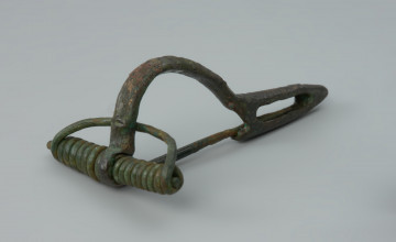 Zapinka z brązu - Ujęcie z przodu z lewej strony. Zapinka z brązu odznaczająca się tzw. „kuszowatą” konstrukcją.