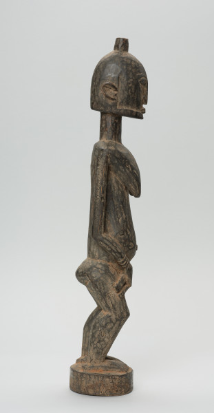 rzeźba - Ujęcie prawego boku. Drewniana, rzeźbiona postać kobiety w pozycji stojącej z dzieckiem ułożonym na lewym biodrze. Głowa stosunkowo duża, tułów zaokrąglony. Oczy, nos (w kształcie strzały), oczy broda lekko zarysowane.