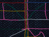 spódnica - Ujęcie środkowego detalu geometrycznego wzoru. Prostokątna spódnica w czarnym kolorze. Wzdłuż utkane kolorowe nitki w kolorach różowym, żółtym białym niebieskim i zielonym. Na środku geometryczny wzór.
