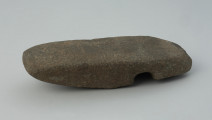 półwytwór, topór - Ujęcie na płasko. Półwytwór topora kamiennego z prostym korpusem, pękniętym w trakcie wiercenia otworu w części tylnej.