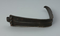 Fragment żelaznej klamry do pasa zdobiony żeberkami - Ujęcie z przodu. Fragment żelaznej klamry do pasa zdobiony żeberkami. Od strony łącznika znajdują się trzy nity.