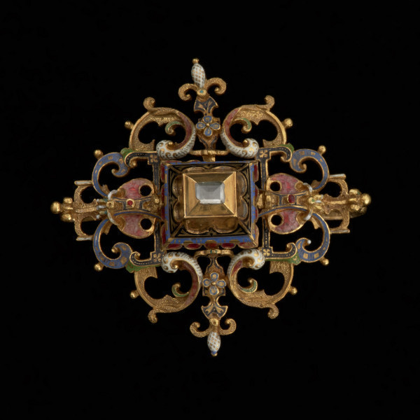 rozeta z kołpaka księcia Filipa II (1573-1618) - Ujęcie z przodu na czarnym tle. Klejnot zbudowany z dwóch skręconych ze sobą śrubą części: ażurowego stelaża o romboidalnym kształcie i osadzonej na nim wysokiej, kasetowej oprawy, ujmującej diament o szlifie tablicowym. Stelaż i ścianki kasztu pokryte barwną emalią, korpusową, a także żłobkową, z wzorami rezerwowanymi w złocie. Rozety mają na spodniej stronie, w narożach, haczyki umożliwiające spinanie ich w łańcuch, a także uszka pozwalające na ich mocowanie do stroju.