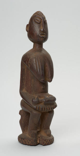 rzeźba - Ujęcie z przodu z prawej strony. Drewniana, rzeźbiona postać z dzieckiem w pozycji siedzącej. Figura pokryta drobnym, dekoracyjnym rytem. Dziecko leżące w pozycji embrionalnej. Ramiona kobiety zaokrąglone.