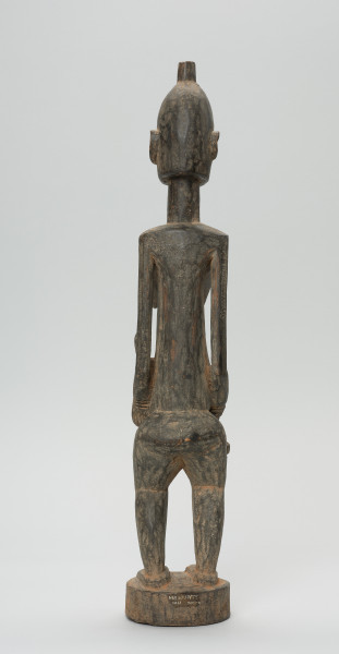 rzeźba - Ujęcie z tyłu. Drewniana, rzeźbiona postać kobiety w pozycji stojącej z dzieckiem ułożonym na lewym biodrze. Głowa stosunkowo duża, tułów zaokrąglony. Oczy, nos (w kształcie strzały), oczy broda lekko zarysowane.