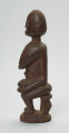 rzeźba - Ujęcie lewego boku. Drewniana, rzeźbiona postać z dzieckiem w pozycji siedzącej. Figura pokryta drobnym, dekoracyjnym rytem. Dziecko leżące w pozycji embrionalnej. Ramiona kobiety zaokrąglone.