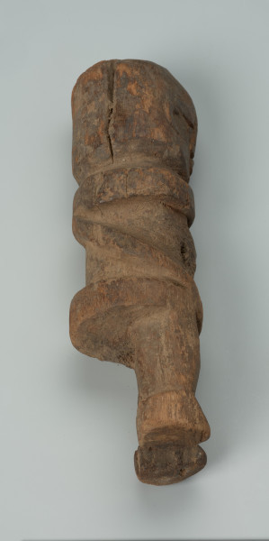 Drewniana figurka mężczyzny z dużą głową - Ujęcie lewej strony w poziomie. Drewniana figurka mężczyzny w pozycji stojącej. Głowa nieproporcjonalnie duża, cała forma uproszczona. Sylwetka masywna.