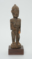 Drewniana figurka kobiety z laską - Ujęcie z przodu. Drewniana figurka kobiety w pozycji stojącej. W prawej dłoni trzyma laskę. Uszkodzona lewa dłoń. Całość pokryta drobnymi wzorami łącznie z włosami upiętymi w kok.
