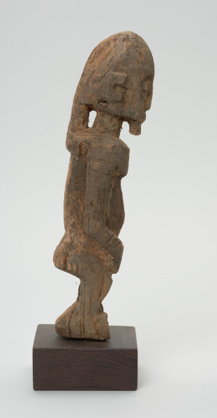 rzeźba - Ujęcie z lewego boku; Figura - postać mężczyzny w pozycji stojącej. O płci świadczy bródka. Części ciała płaskorzeźbione z bryły. Forma uproszczona, zgeometryzowana. Związana z kultem przodków, przeznaczona na ołtarz przodków.