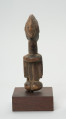 rzeźba - Ujęcie z tyłu. Figura przedstawiająca postać kobiety. Duża głowa, z zaznaczoną fryzurą, ręce prostymi cięciami wydobyte z tułowia. Figura kanoniczna. Brak nóg. Związana z kultem przodków.
