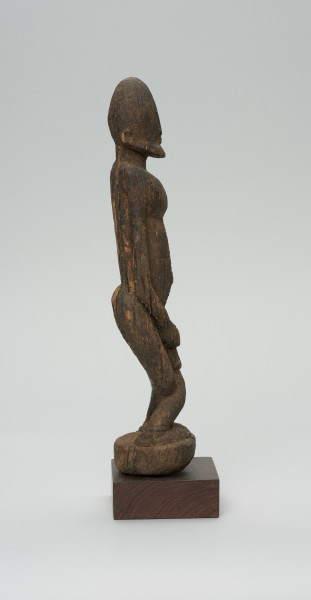 rzeźba - Ujęcie prawego boku. Figura przedstawiająca postać przodka -  mężczyznę ze skrzyżowanymi nogami. Figura antropomorficzna, oddająca cechy dogońskiego kanonu przedstawiania ludzi.