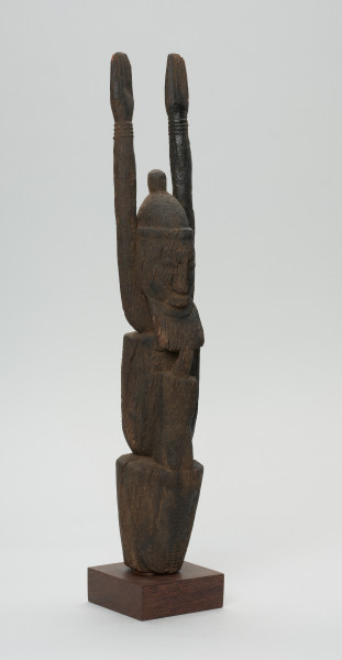 rzeźba - Ujęcie z przodu z prawej strony. Figurka przedstawia Hogona – kapłana kultu Lebe. Widoczna broda, wyprostowane ręce uniesione do góry.