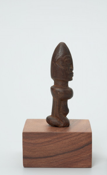 rzeźba - Ujęcie z boku; Figura - postać przodka przedstawiająca przodka w pozycji siedzącej (klęczącej?) na ugiętych w kolanach nogach. Głowa duża, ok. ? powierzchni figurki. Wyraźnie zaznaczone rysy 