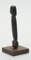Drewniana figurka postaci z długim tułowiem - Ujęcie z lekkim odchyleniem na prawo; drewniana figurka postaci ludzkiej przedstawionej schematycznie. Całość wygładzona, zarysowana głowa i długi tułów.