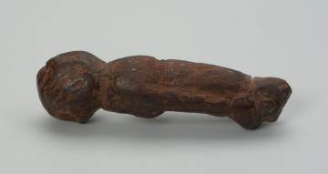Drewniana figurka zwierzęcia - Ujęcie lewego boku, w poziomie. Drewniana figurka zwierzęcia. Forma bardzo uproszczona, z bryły symbolicznie wyodrębnione: głowa, tylne i przednie kończyny oraz ogon.