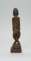 rzeźba - Ujęcie z tyłu. Figura przedstawiająca postać przodka -  mężczyznę ze skrzyżowanymi nogami. Figura antropomorficzna, oddająca cechy dogońskiego kanonu przedstawiania ludzi.