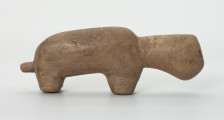 Drewniana figura zwierzęcia z krótkim ogonem - Ujęcie z prawej strony. Drewniana figurka nieokreślonego zwierzęcia z długą szyją, podłużną głową i krótkim ogonem.