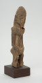 rzeźba - Ujęcie ze skosu z lewej; Figura - postać mężczyzny w pozycji stojącej. O płci świadczy bródka. Części ciała płaskorzeźbione z bryły. Forma uproszczona, zgeometryzowana. Związana z kultem przodków, przeznaczona na ołtarz przodków.