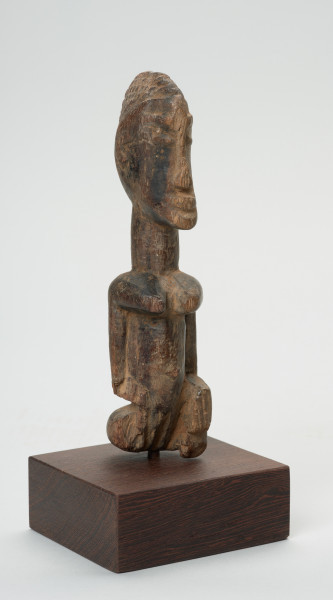 rzeźba - Ujęcie z przodu z prawej strony. Figura przedstawiająca postać kobiety. Duża głowa, z zaznaczoną fryzurą, ręce prostymi cięciami wydobyte z tułowia. Figura kanoniczna. Brak nóg. Związana z kultem przodków.