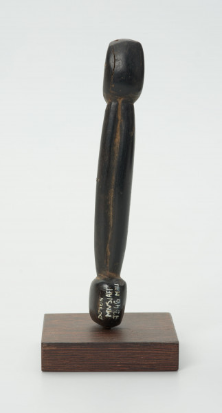 Drewniana figurka postaci z długim tułowiem - Ujęcie z tyłu; drewniana figurka postaci ludzkiej przedstawionej schematycznie. Całość wygładzona, zarysowana głowa i długi tułów.