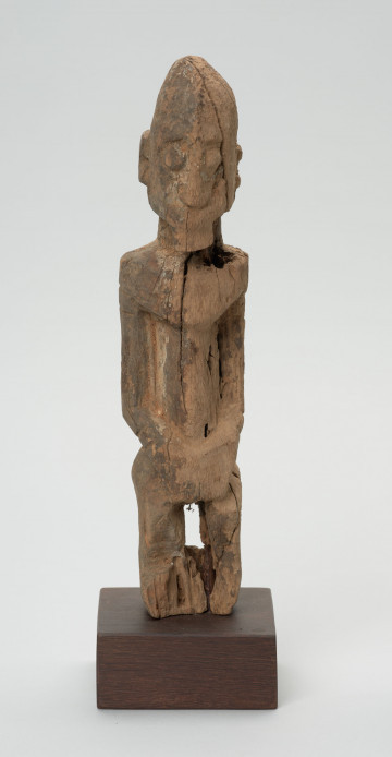 rzeźba - Ujęcie z przodu; Figura - postać mężczyzny w pozycji stojącej. O płci świadczy bródka. Części ciała płaskorzeźbione z bryły. Forma uproszczona, zgeometryzowana. Związana z kultem przodków, przeznaczona na ołtarz przodków.