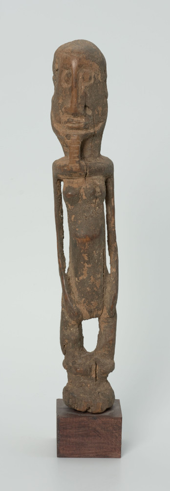 Drewniana figurka androgyniczna - Ujęcie z przodu; drewniana figurka przedstawiająca postać z brodą i piersiami. Statyczna, zgeometryzowana. Ręce wyodrębnione z tułowia.