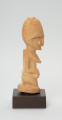 rzeźba - Ujęcie prawego boku. Figurka przedstawiająca kobietę siedzącą na podkulonych nogach. Głowa duża, reszta postaci wydobyta płytkimi nacięciami. Forma zgeometryzowana.