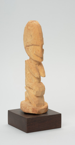 rzeźba - Ujęcie z przodu z prawej strony. Figurka przedstawiająca kobietę siedzącą na podkulonych nogach. Głowa duża, reszta postaci wydobyta płytkimi nacięciami. Forma zgeometryzowana.