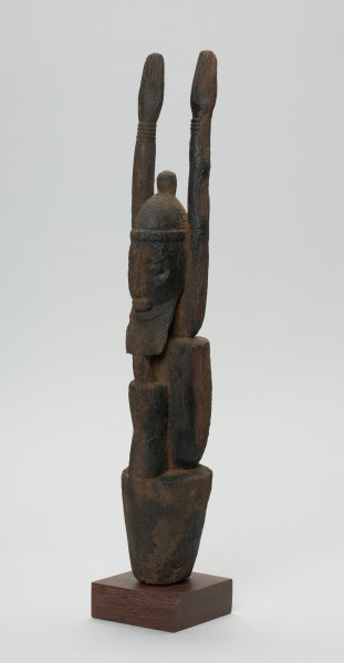 rzeźba - Ujęcie z przodu z lewej strony. Figurka przedstawia Hogona – kapłana kultu Lebe. Widoczna broda, wyprostowane ręce uniesione do góry.