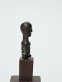 Mała drewniana figurka przedstawiająca popiersie człowieka - Ujęcie z prawej strony; Mała drewniana figurka przedstawiająca popiersie człowieka. Głowa i tułów starannie wygładzone. Postać ujęta schematycznie. Głowa, rysy, piersi, ręce, wydobyte płytkimi nacięciami.