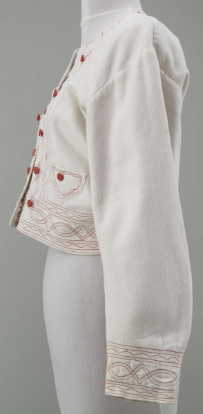 Kaftan kobiecy wykonany z tkaniny bawełnianej (piki), koloru białego. Ozdobiony stebnówką koloru czerwonego i zielonego oraz czerwonymi guzikami. Na lnianej podszewce.