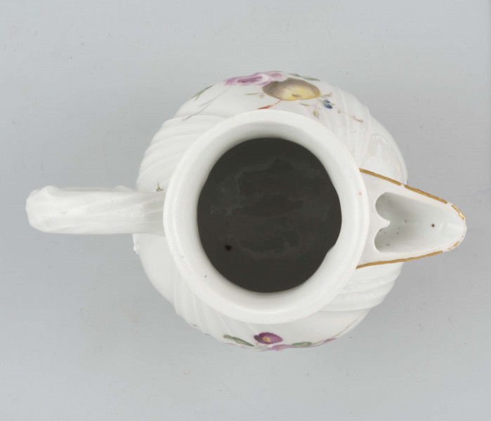 Dzbanek gruszkowaty na pierścieniowej podstawie, uchwyt okrągły z liściastymi ornamentami w osadzeniach, wylew z dziobkiem. Pokrywka kopulasto wysklepiona z uchwytem w kształcie pączka róży. Powierzchnia ukośnie kanelowana z plecionką wokół górnej krawędzi  - w typie Neu Ozier,  podobnie opracowana pokrywka, Na brzuścu wielobarwna dekoracja w formie pęków kwiatów, owoców i warzyw; po jednej stronie: stokrotki, marchew i filetowa śliwka, po drugiej - róża i żółta śliwka. Na pokrywce drobne gałązki kwiatowe.
 