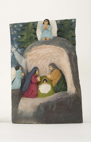 Płaskorzeźba z drewna topolowego przedstawiająca szopkę. W grocie przypominającej stajenkę, na środku umieszczony jest Jezus z żłóbku. Z prawej strony klęczy Matka Boska i aniołek, z lewej – św. Józef. Nad grotą drugi aniołek. W tle zielone drzewa. Na ciemnogranatowym niebie białe gwiazdki i Gwiazda Betlejemska. Wnętrze groty pomalowane jest różową farbą. Jezus leży na zielonym sianie przykrytym białą pieluszką. MB ubrana jest w suknię czerwoną, na głowie ma ciemnoniebieski welon. Św. Józef ma szatę żółtą, okrytą ciemnozielonym płaszczem. Aniołki występują w sukniach jasnoniebieskich. Skrzydła mają białe. Twarze postaci o wyraźnie zaznaczonych oczach, nosach i ustach, niemalowane. Kompozycja malowana farbami plakatowymi, pociągnięta lakierem bezbarwnym. 