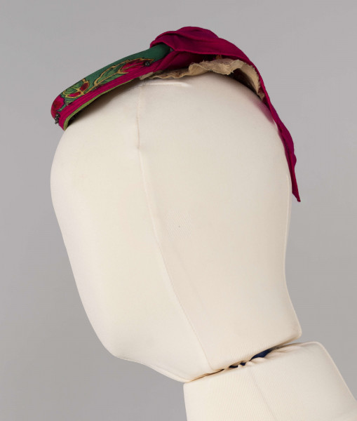 E/668/ML - Strój głowy mężatki wykonany z chustki fabrycznej koloru różowego w kwiatki, zawiązany na drewnianej obręczy. Przybrany paciorkami założonymi na szpilki.