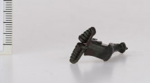 1834/A/ML/1 - Fibula brązowa z poprzecznie żłobkowanym grzebieniem na kabłąku, górną cięciwą i 13-to zwojową sprężyną. Nóżka fibuli zakończona stożkowatym guzkiem. Pochewka płaska, szeroka, delikatnie zawinięta.