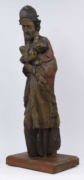 E/17554/ML - Rzeźba drewniana, pełna, z resztkami polichromii, przedstawiająca św. Józefa z Dzieciątkiem. Kompozycja frontalna. Postać stojąca, ubrana w długą szatę wykończoną ozdobną szatę wykończoną ozdobną koronką przy rękawach, drapowane w pionowe fałdy. Na ramionach  płaszcz, również wykończony koronką. Tył postaci modelowany gładko. Prawa ręka, wyciągnięta wzdłuż ciała, trzyma kwiat, który wystaje ponad ramię. Na lewej zgiętej ręce – Dzieciątko, które prawą ręką trzyma się szyi św. Józefa. Dzieciątko nagie, w pieluszkach. 
Twarz świętego skierowana w stronę Dzieciątka, pochylona w prawo. Pociągła. Nos posty. Usta lekko zaznaczone. Oczy lekko przymknięte. Bruzdy na czole i policzkach, misterne pukle brody i włosów. Na głowie rodzaj czapki, ściśle przylegającej. Postać świętego bez stóp. Liczne spękania i ubytki fragmentów.

Konserwacja: 1988 r.