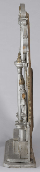 E/7373/ML - Ołtarzyk składa się z 3 części: podstawy i 2 pięter. Oba piętra podzielone na 3 pola (środkowe 24 cm, boczne 13,5 cm) przez kolumny. Podstawa posiadająca wysuniętą część środkową, ozdobiona jest 4 krzyżami greckimi wpisanymi w gwiazdę złot. Podstawę flankują 2 małe ołtarzyki: prawe brak przedstawienia, po lewej Madonna – złota postać na owalnym srebrnym polu, z granatową aureolą, nad nią na granatowym tle – 4 złote gwiazdki. Prawy ołtarzyk nad brakującym przedstawieniem ma złotą gwiazdkę. Lewemu jej brak. Górne pole podstawy zdobią 2 kolumienki oraz złote guzy pomiędzy. 
I piętro w części środkowej, pomiędzy kolumnami z tympanonem z głową aniołka i klęczącymi aniołami na daszku, postać Chrystusa Ukrzyżowanego w kolorze srebrnym, wraz ze złotymi  inskrypcją i pionowymi ząbkami. Po bokach, symetrycznie, przedstawienia  św. Mikołaja w złotej czapce biskupiej, na owalnej podstawie, z jedną ręką uniesioną , a druga opuszczoną trzymającą rękojeść. Ponad stylizowany złoty ornament roślinny. Całość piętra flankowana ornamentem przypominającym liście akantu i ślimacznice. 
II piętro w częściach bocznych zamknięte jest spływami wolutowymi , na polach po złotej kolumience/sterczynie i gwieździe. W części środkowej oleodruk ze św. Józefem z Dzieciątkiem, w złotej ramce. Całość wieńczą postaci ornatów w kolorze srebrnym i złote niepełne spływy wolutowe ze ślimacznicą. 
Brak wielu elementów. Plecy ołtarzyka stanowi 6 deseczek o szer. 10,5 cm i grubości 1,2 cm.