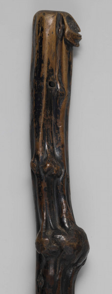 E/1651/ML - Laska drewniana z jednego kawałka drewna; zachowane naturalne wyżłobienia i pozostałości po konarach, tworzące ozdobne guzy. Główka laski spłaszczona, z wyrzeźbioną antropomorficzną twarzą z zaznaczonymi oczami, nosem i ustami. Koniec laski zwężony, zakończony elementem walcowatym oraz ostro zakończonym wielobokiem. Laska politurowana pierwotnie, następnie malowana na całej powierzchni - pozostałości czarnej farby.