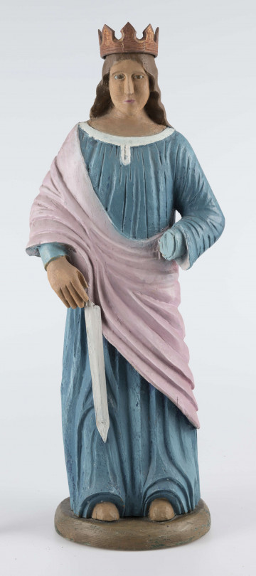 E/16790/ML - Rzeźba drewniana pełna polichromowana, przedstawiająca św. Katarzynę. Postać stojąca, ubrana w niebieską (wcześniej kolor ultramaryny) suknię, żłobioną  w fałdy, z białym wykończeniem przy szyi. Na wierzch, na prawe ramię, narzucony płaszcz/szal w kolorze jasnoróżowym. Prawa ręka opuszczona, trzyma miecz (obecnie samo ostrze koloru białego), lewa zgięta jest w łokciu – brak partii dłoni. Odsłonięte części ciała (stopy, dłonie, szyja, twarz) w kolorze jasnobrązowym; wcześniej prawdopodobnie beżowo-kremowe. Twarz owalna, brązowo-błękitne gałki oczne, usta różowe. Włosy brązowe, spływające fałdami do połowy pleców. Na głowie korona z 8 wierzchołkami, żłobiona, brązowa, uszlachetniona złotą farbą. 
Postać stoi na owalnej podstawie (22 x 19 cm), o wys. 3,5 cm, pomalowanej na brązowo (umbra), wcześniej – w szmaragdowej zieleni.