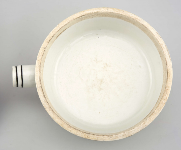 Naczynie stożkowate z uchwytem w postaci szerokiej rurki (służącym do zamocowania drewnianej rączki), pokrywa kopulasta z uchwytem w kształcie rozkwitłej korony kwiatowej. Krawędzie obwiedzione czarnymi paskami, czernią podkreślony modelunek uchwytu. Spód nieszkliwiony.
 