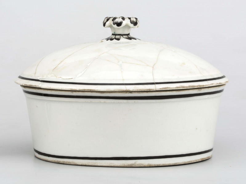 Naczynie stożkowate z uchwytem w postaci szerokiej rurki (służącym do zamocowania drewnianej rączki), pokrywa kopulasta z uchwytem w kształcie rozkwitłej korony kwiatowej. Krawędzie obwiedzione czarnymi paskami, czernią podkreślony modelunek uchwytu. Spód nieszkliwiony.
 